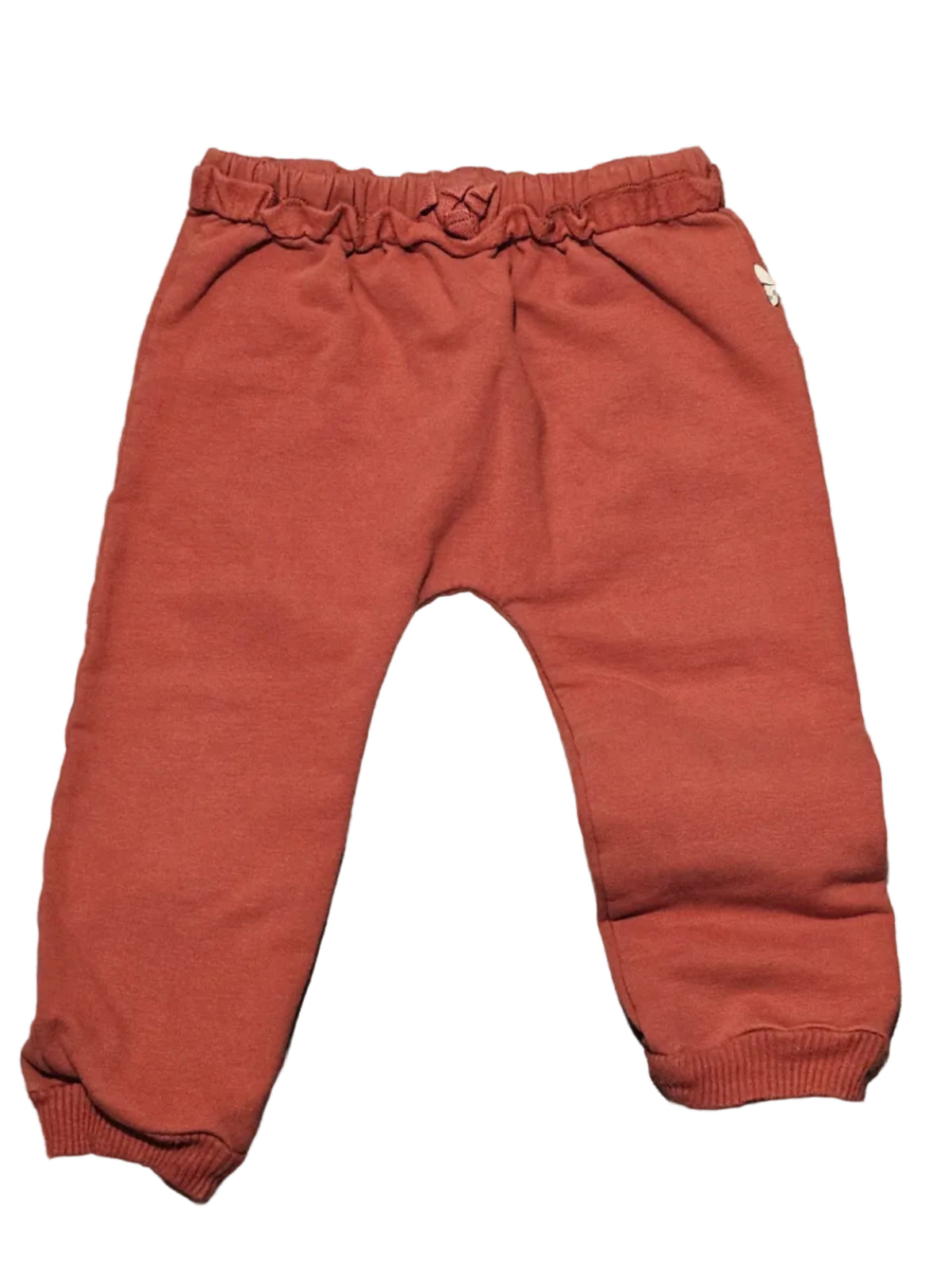 A pair of toddler's rust-orange sweatpants with an elastic waistband and cuffed ankles, laid flat on a gray wood-look floor.